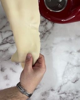 Una persona tiene in mano un pezzo di impasto davanti a un'impastatrice.