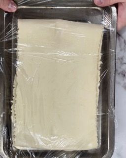 Una persona tiene in mano un vassoio di cibo avvolto in pellicola trasparente.