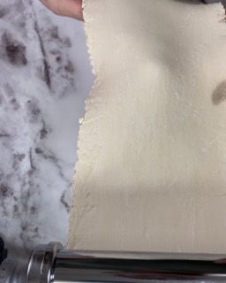 Una persona sta stendendo un pezzo di pasta su un mattarello.