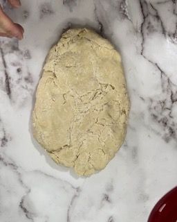 Una persona tiene in mano un pezzo di pasta su una superficie di marmo.