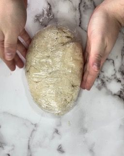 Una persona tiene in mano una palla di pasta avvolta nella pellicola trasparente.