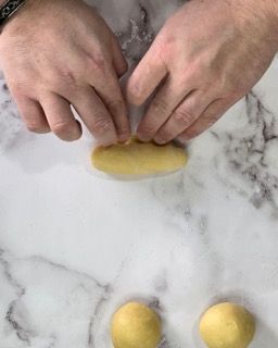 Una persona tiene in mano un pezzo di pasta su un tavolo.