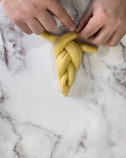 Una persona sta realizzando una treccia con l'impasto su una superficie di marmo.