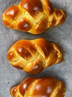 Tre rotoli di challah sono appoggiati su un pezzo di carta oleata.