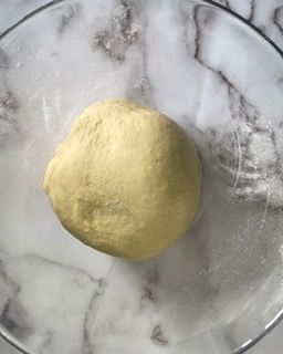 Una palla di pasta è appoggiata su un piatto di vetro su una superficie di marmo.