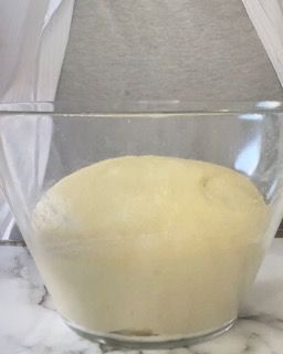 Una ciotola di vetro piena di impasto è appoggiata su un tavolo.