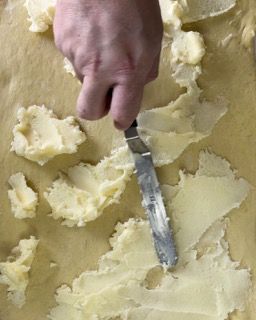 Una persona sta spalmando il burro su un pezzo di pasta con una spatola.