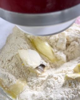 Primo piano di una ciotola di farina e burro mescolati in una planetaria.