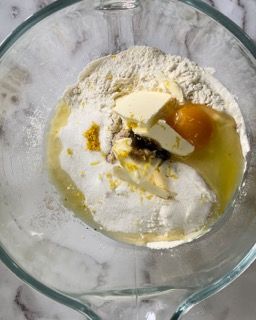 Una ciotola di vetro piena di farina, burro e un uovo.