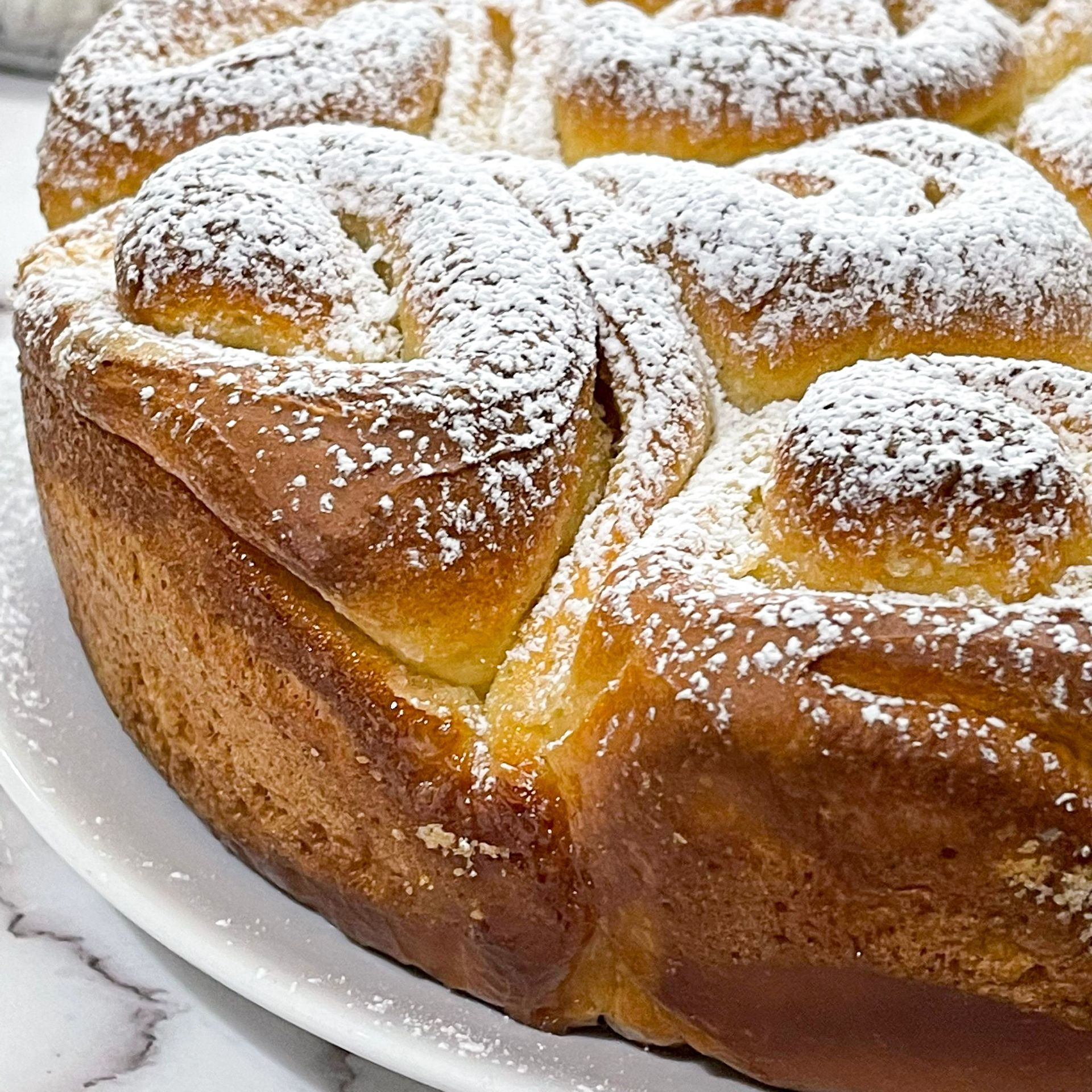 Una pagnotta di pane con zucchero a velo sopra è su un piatto bianco.