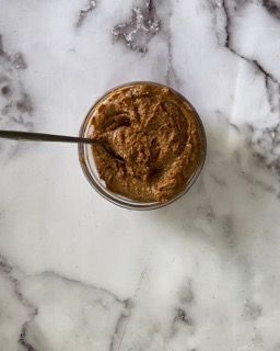 Un barattolo di burro di arachidi con un cucchiaio dentro su una superficie di marmo.