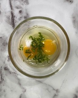 Una ciotola di vetro piena di uova e cipolle verdi su un tavolo.