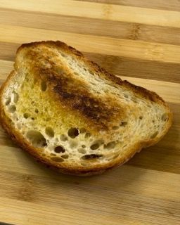 Una fetta di pane tostato è appoggiata su un tagliere di legno.