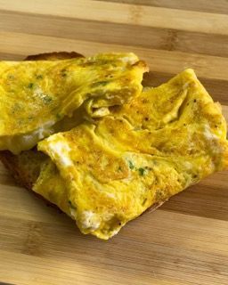 Primo piano di una frittata su pane tostato su un tagliere di legno.