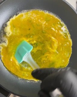 Una persona sta cuocendo le uova in una padella con una spatola.