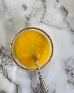 Una ciotola di salsa gialla con un cucchiaio dentro su una superficie di marmo.