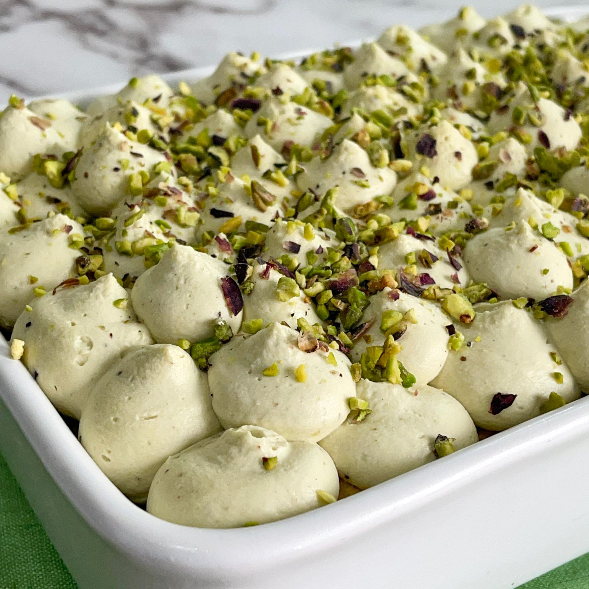 Una teglia bianca ripiena di panna montata e pistacchi.