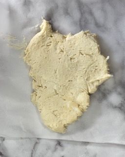 Un pezzo di pasta è appoggiato su un foglio di carta oleata su una superficie di marmo.