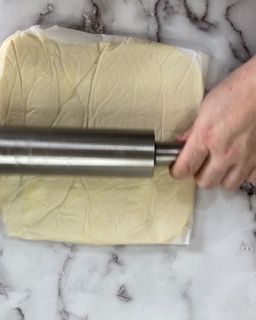 Una persona sta stendendo la pasta con un mattarello su una superficie di marmo.