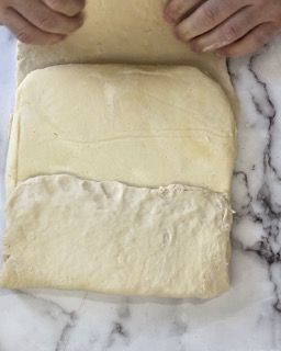 Una persona tiene in mano un pezzo di pasta su una superficie di marmo.