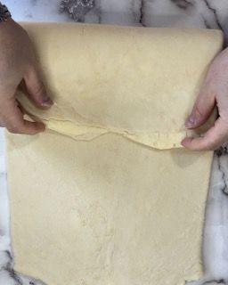 Una persona sta stendendo un pezzo di pasta su un bancone di marmo.