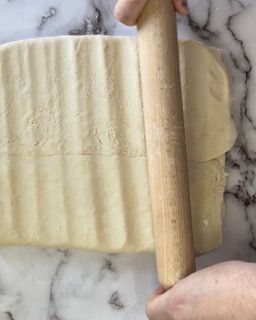 Una persona sta stendendo un pezzo di pasta con un mattarello.