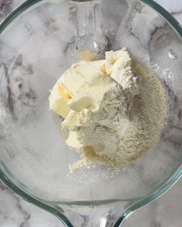 Una ciotola di vetro piena di farina e burro su un tavolo.