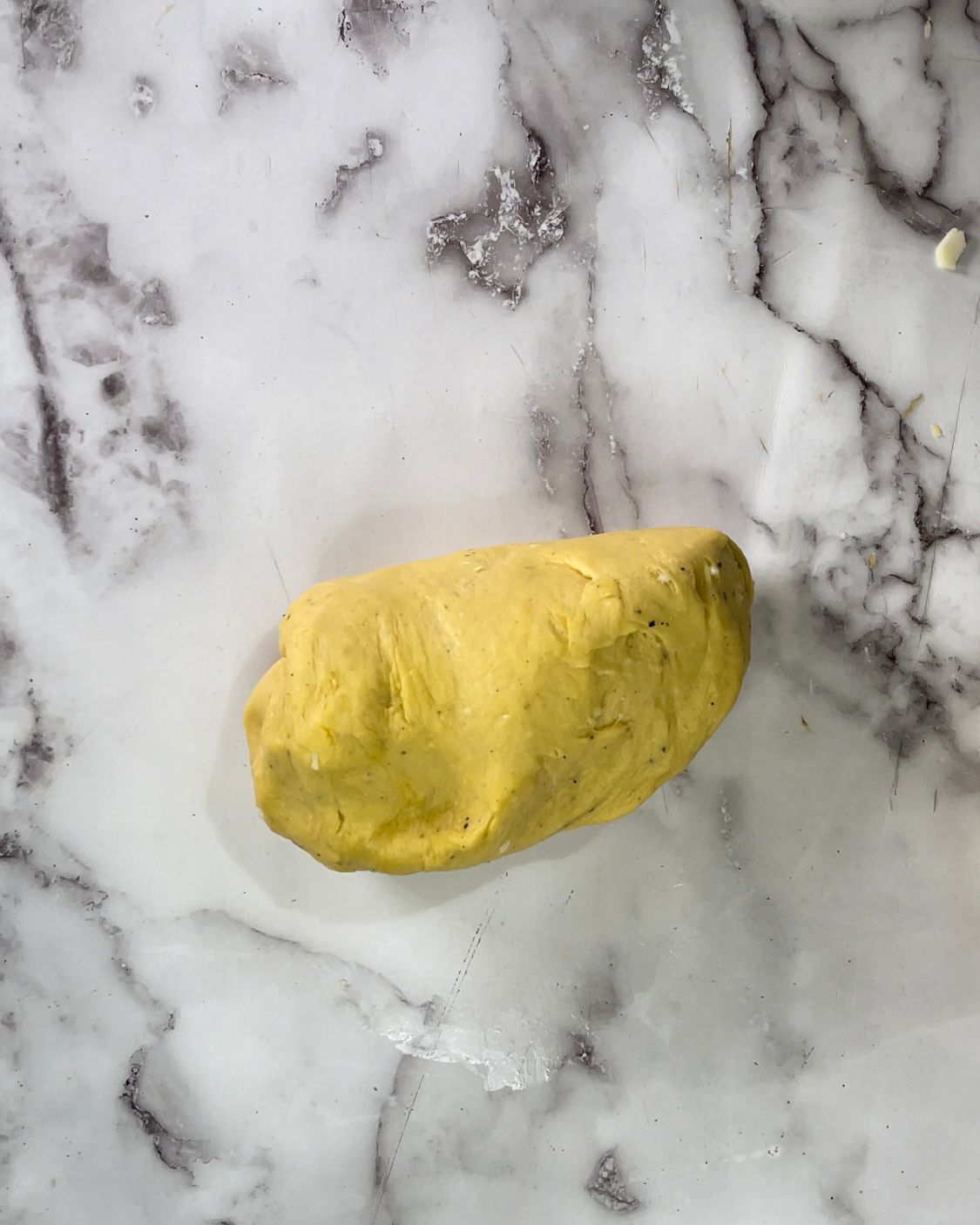 Un pezzo di pasta gialla è appoggiato su una superficie di marmo.
