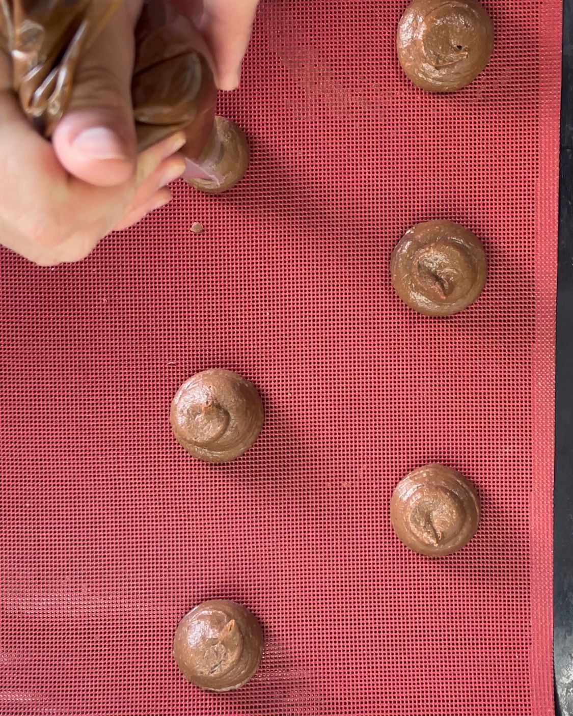 Una persona sta preparando dei biscotti al cioccolato su un tappetino rosso.