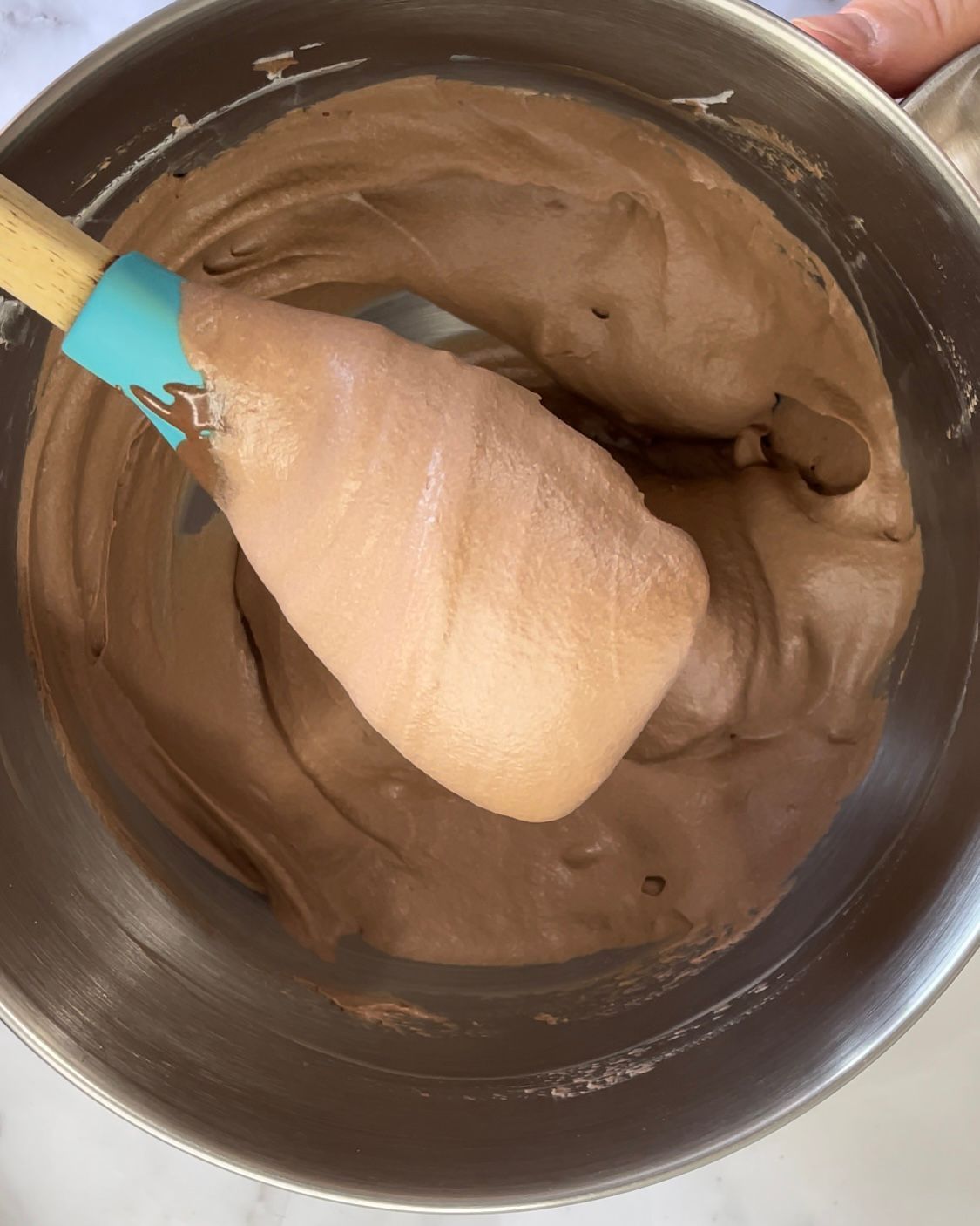 Una persona tiene in mano una spatola in una ciotola piena di glassa al cioccolato.