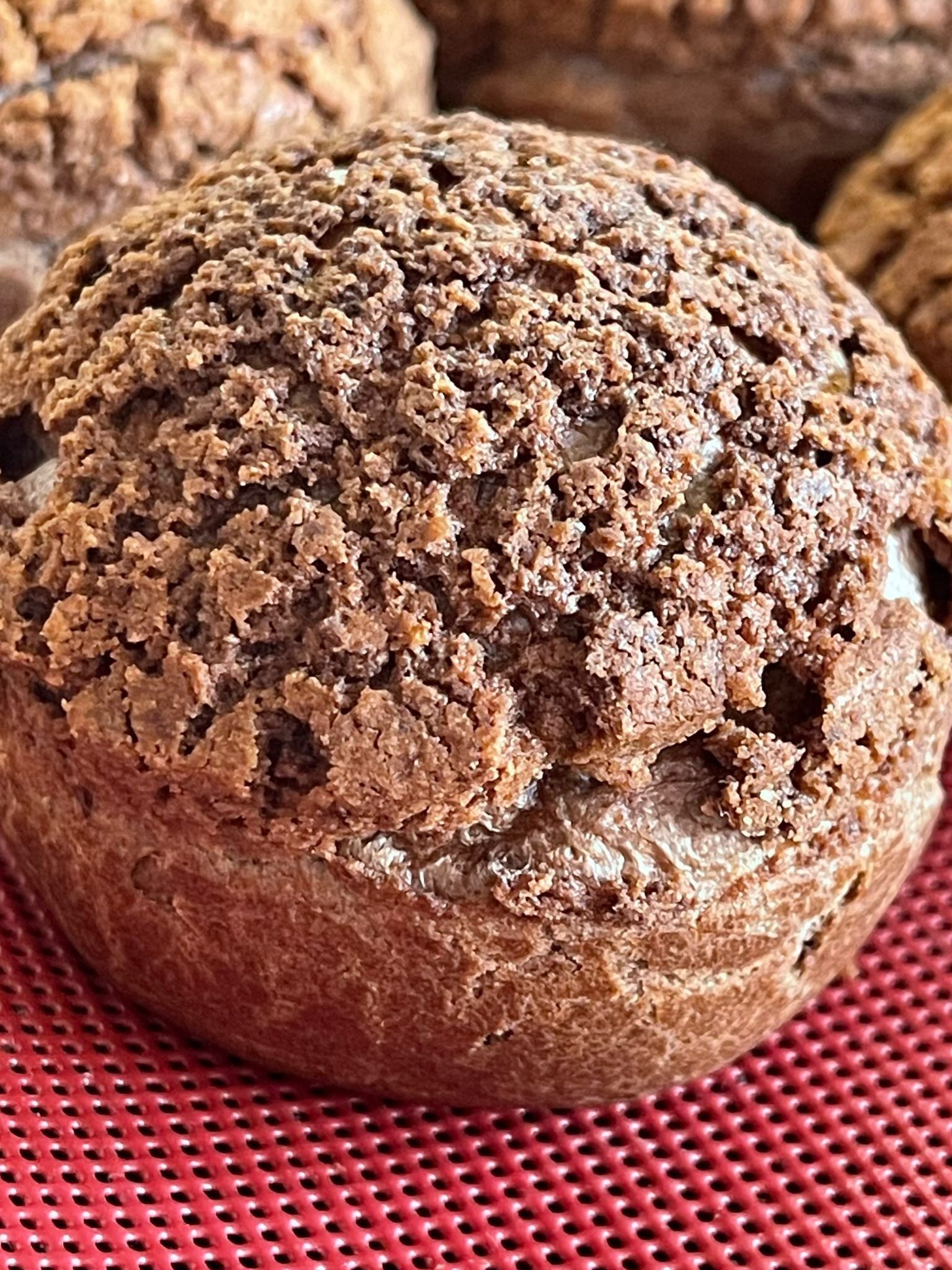 Primo piano di un muffin al cioccolato su una superficie rossa.