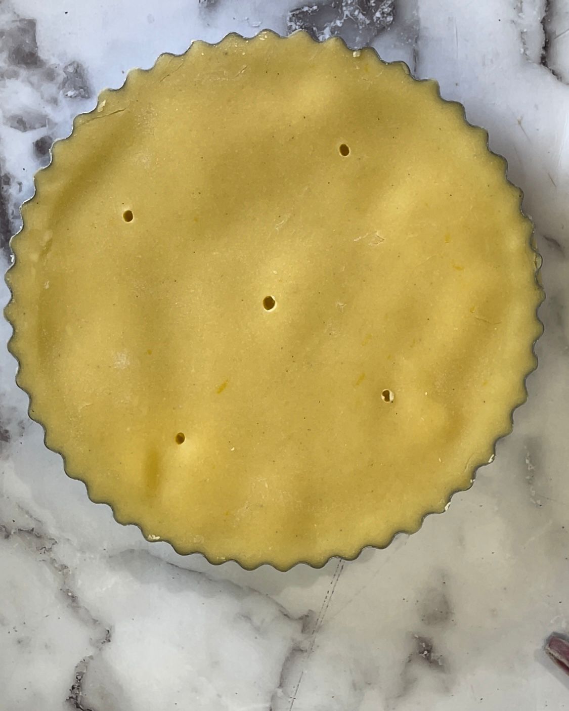 Una crosta di torta con dei buchi è appoggiata su una superficie di marmo