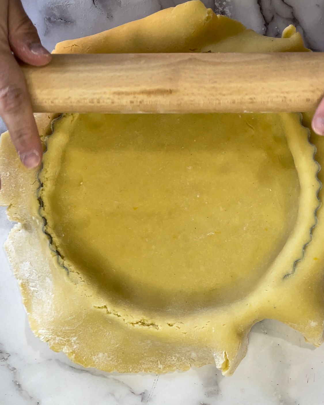 Una persona sta stendendo la pasta per una torta con un mattarello.
