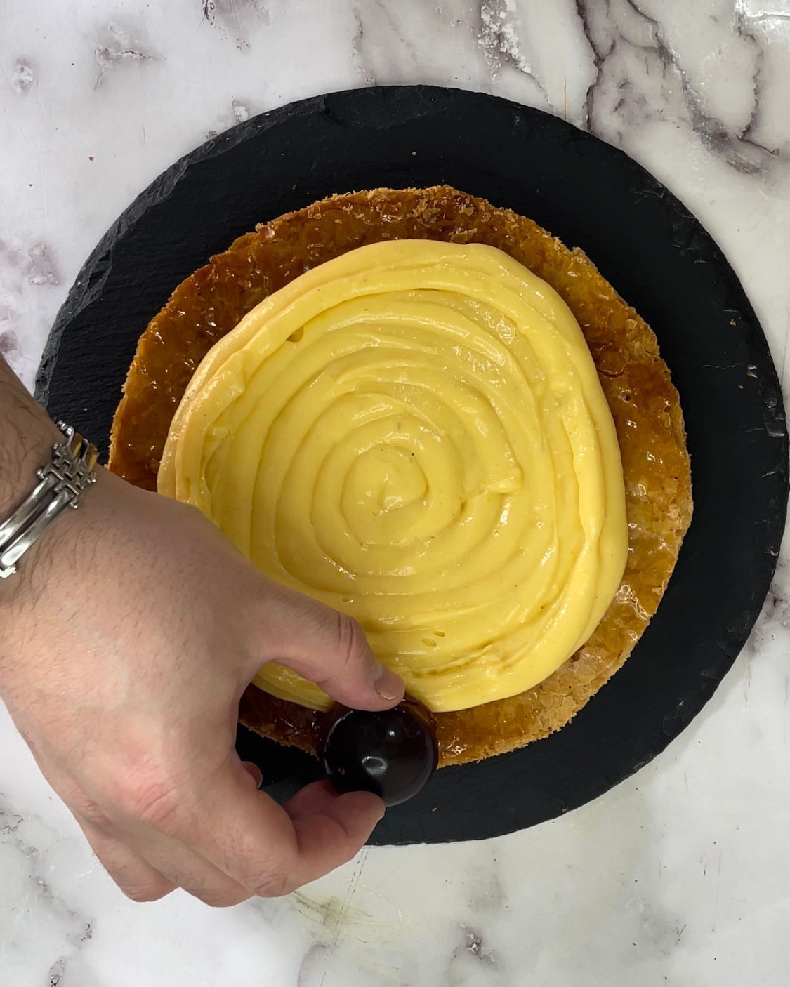 Una persona tiene in mano una ciliegia in cima a una torta con glassa gialla