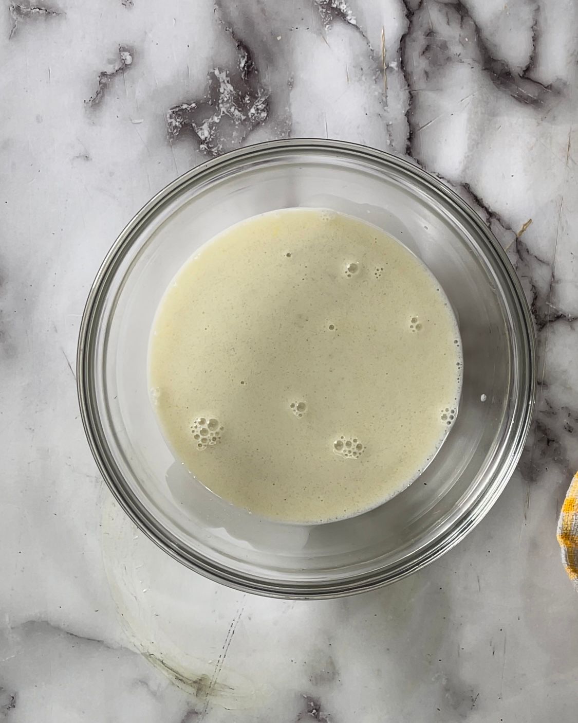 Una ciotola di vetro piena di un liquido bianco su una superficie di marmo.