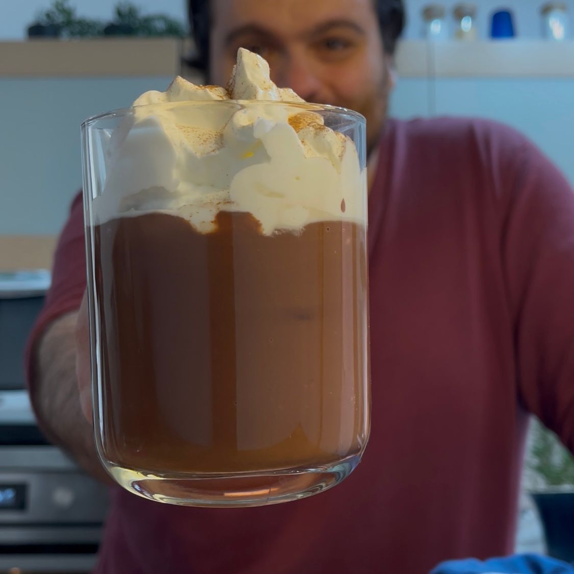 Un uomo tiene in mano un bicchiere di budino al cioccolato con panna montata sopra.