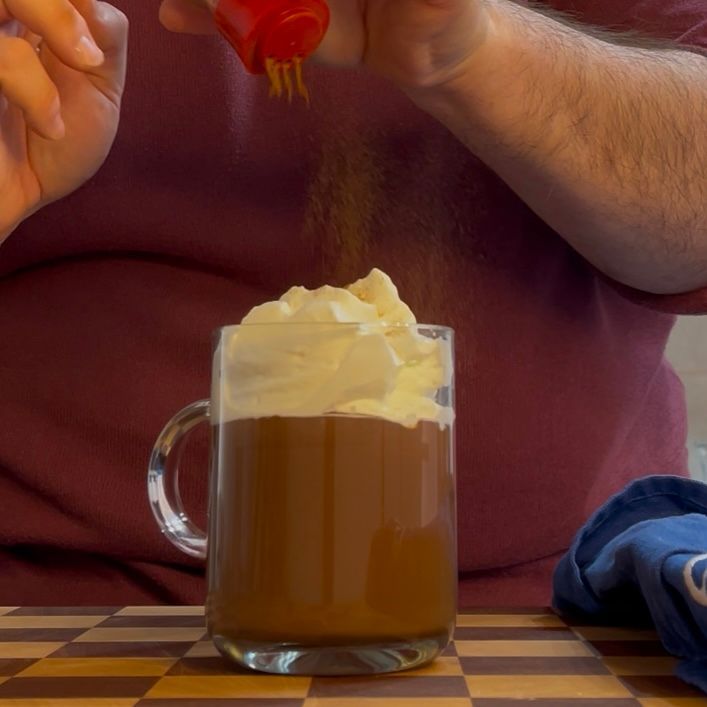 Un uomo versa il ketchup in una tazza di caffè con panna montata
