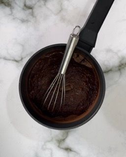 Una frusta è in una pentola di salsa al cioccolato.