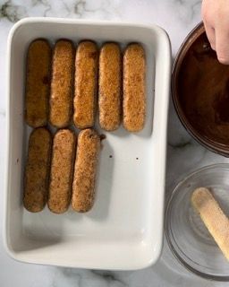 Una teglia bianca piena di biscotti al tiramisù accanto a una ciotola di salsa al cioccolato.