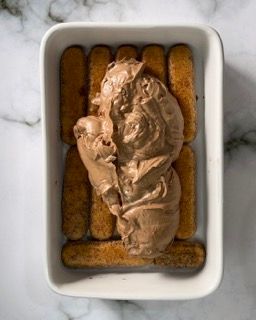 Una pirofila bianca piena di gelato al cioccolato e biscotti.