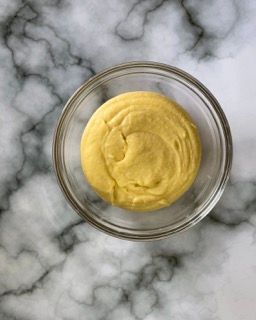 Una ciotola di vetro piena di salsa gialla su una superficie di marmo.