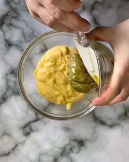 Una persona sta versando la salsa verde in una ciotola di vetro.