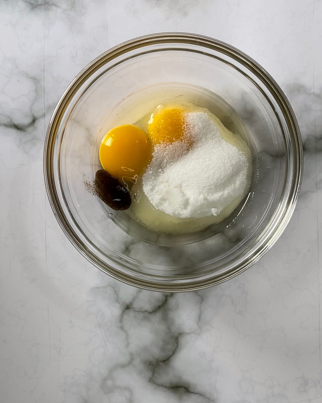 Una ciotola di vetro piena di uova e zucchero su un tavolo