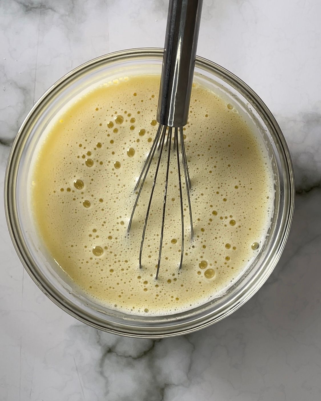 Una frusta è in una ciotola di liquido su un tavolo.