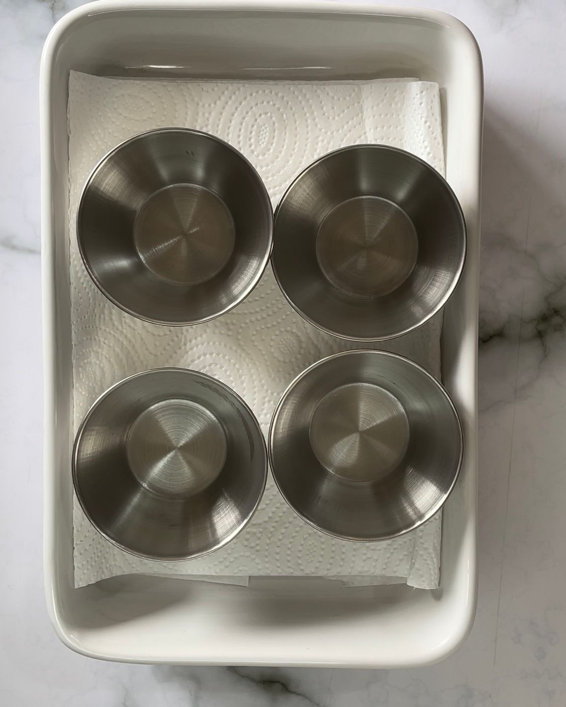 Quattro ciotole di metallo sono appoggiate su un tovagliolo di carta in un contenitore bianco.