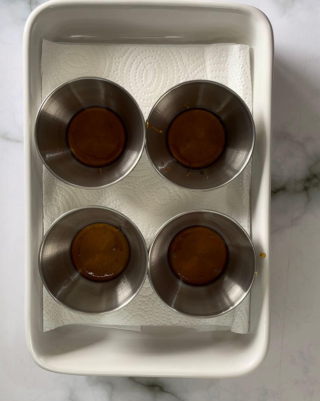 Quattro tazze di metallo piene di liquido marrone sono appoggiate su un tovagliolo di carta.