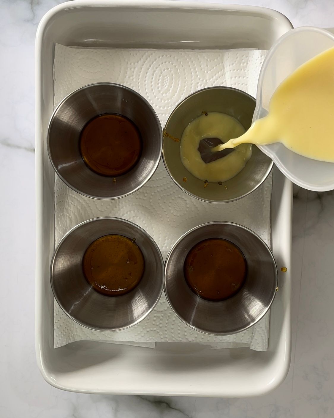 Una casseruola bianca contenente quattro ciotole di metallo riempite con liquidi di colore diverso.