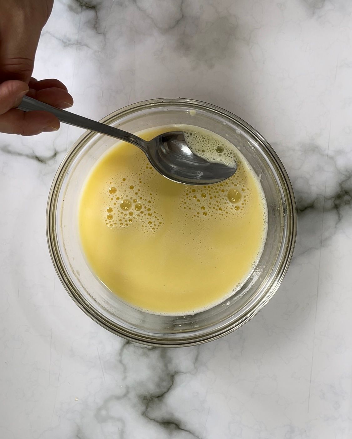 Una persona tiene in mano un cucchiaio in una ciotola piena di liquido.