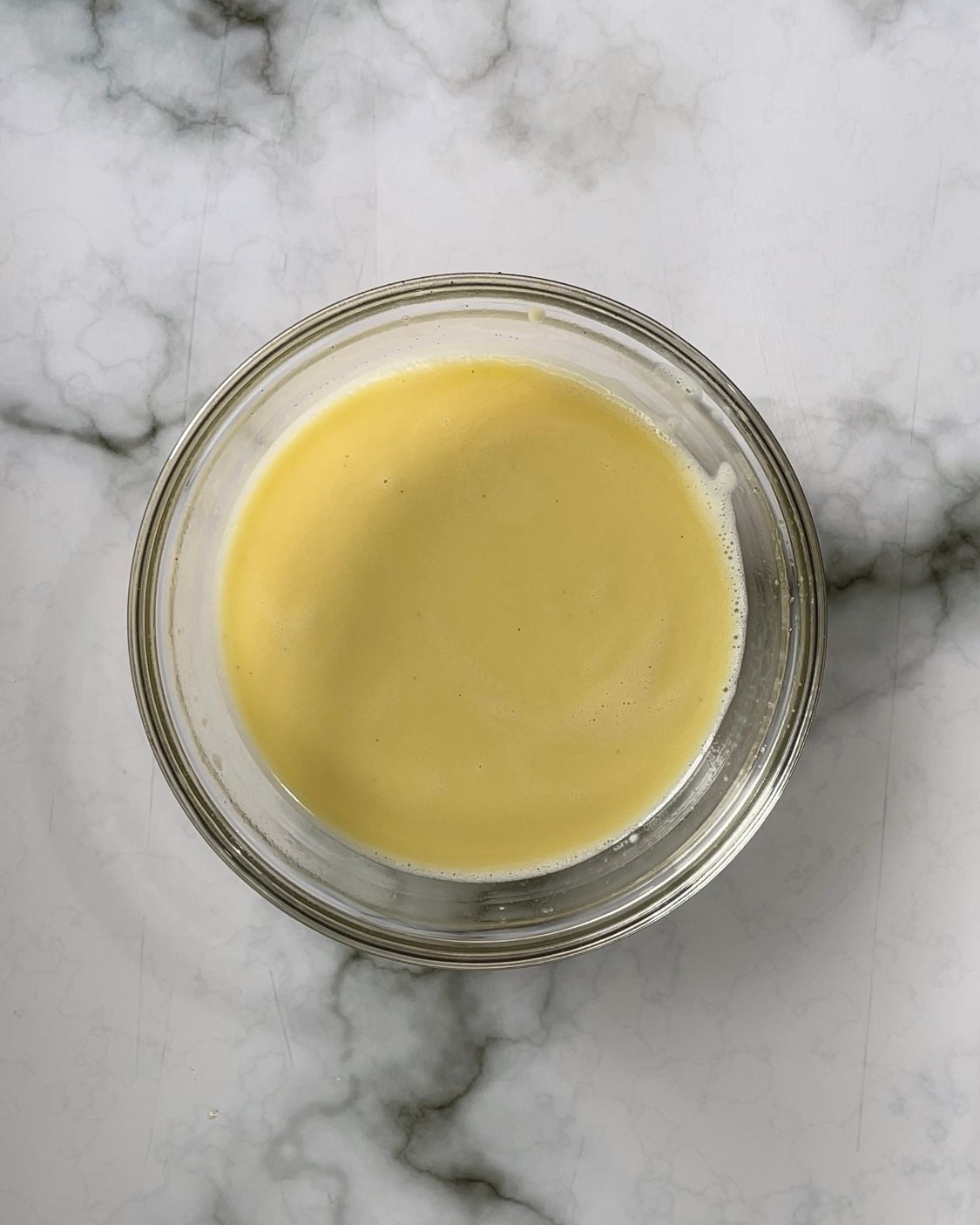 Una ciotola piena di liquido giallo è appoggiata su una superficie di marmo.