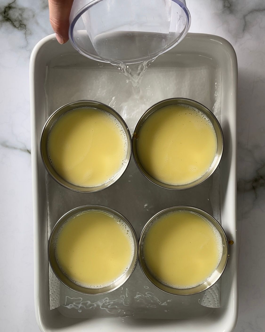 Una persona versa del liquido in una pentola contenente quattro tazze di crema pasticcera.